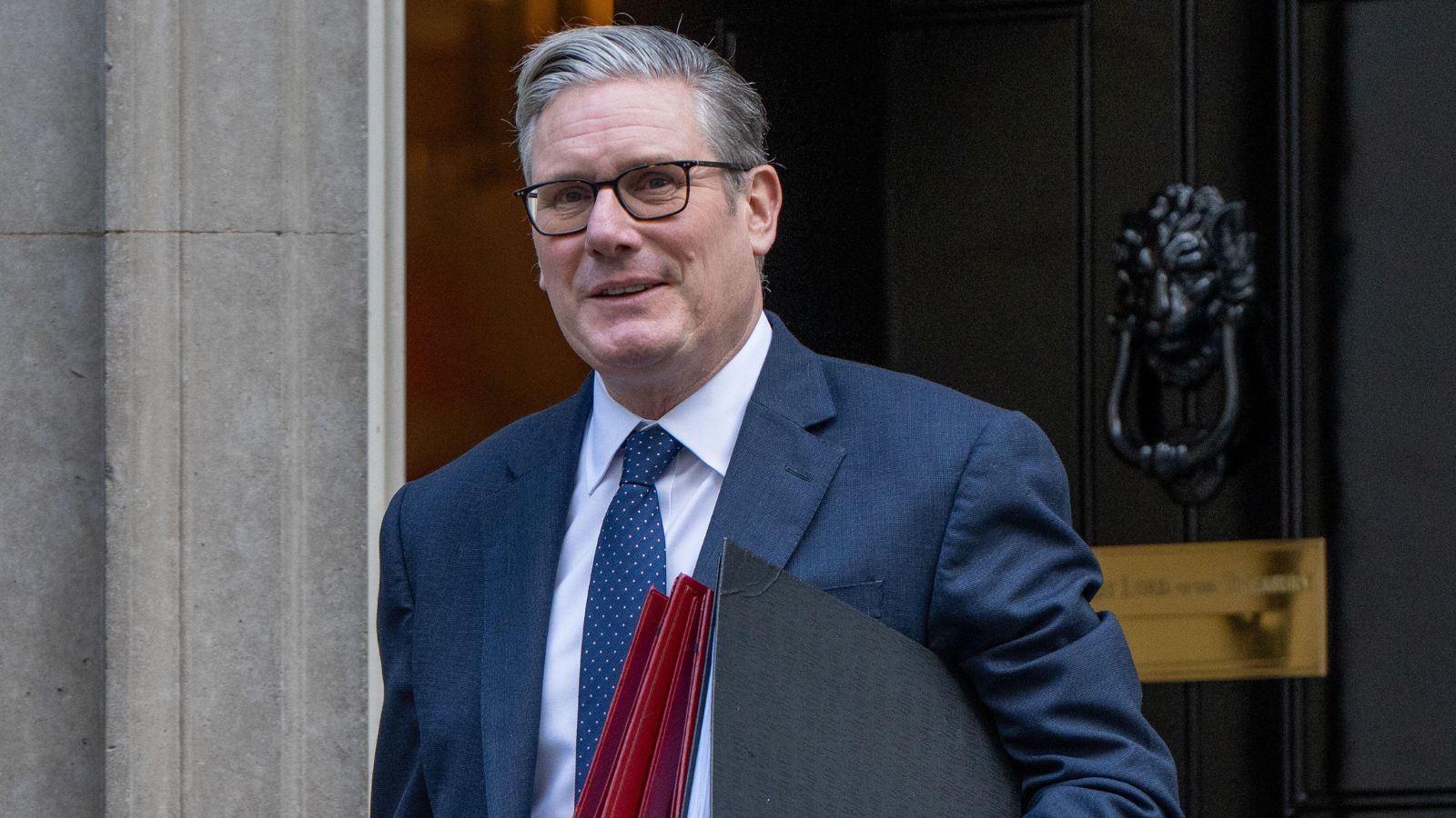 Incumbent Prime Minister Keir Starmer carries a stack of folders outside 10 Downing Street, smiling