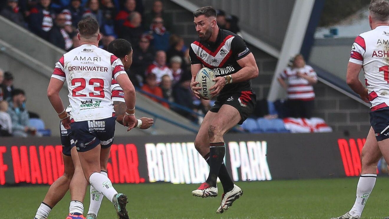 Will Lovell in action for London Broncos in 2025, running the ball in at numerous Oldham defenders during a Championship clash at Boundary Park