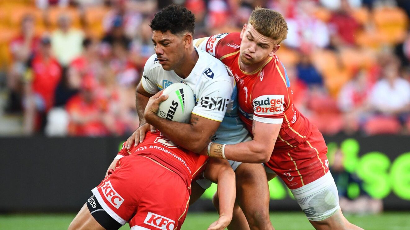 Brian Kelly in action for Gold Coast Titans in 2025, being tackled by two Dolphins defenders