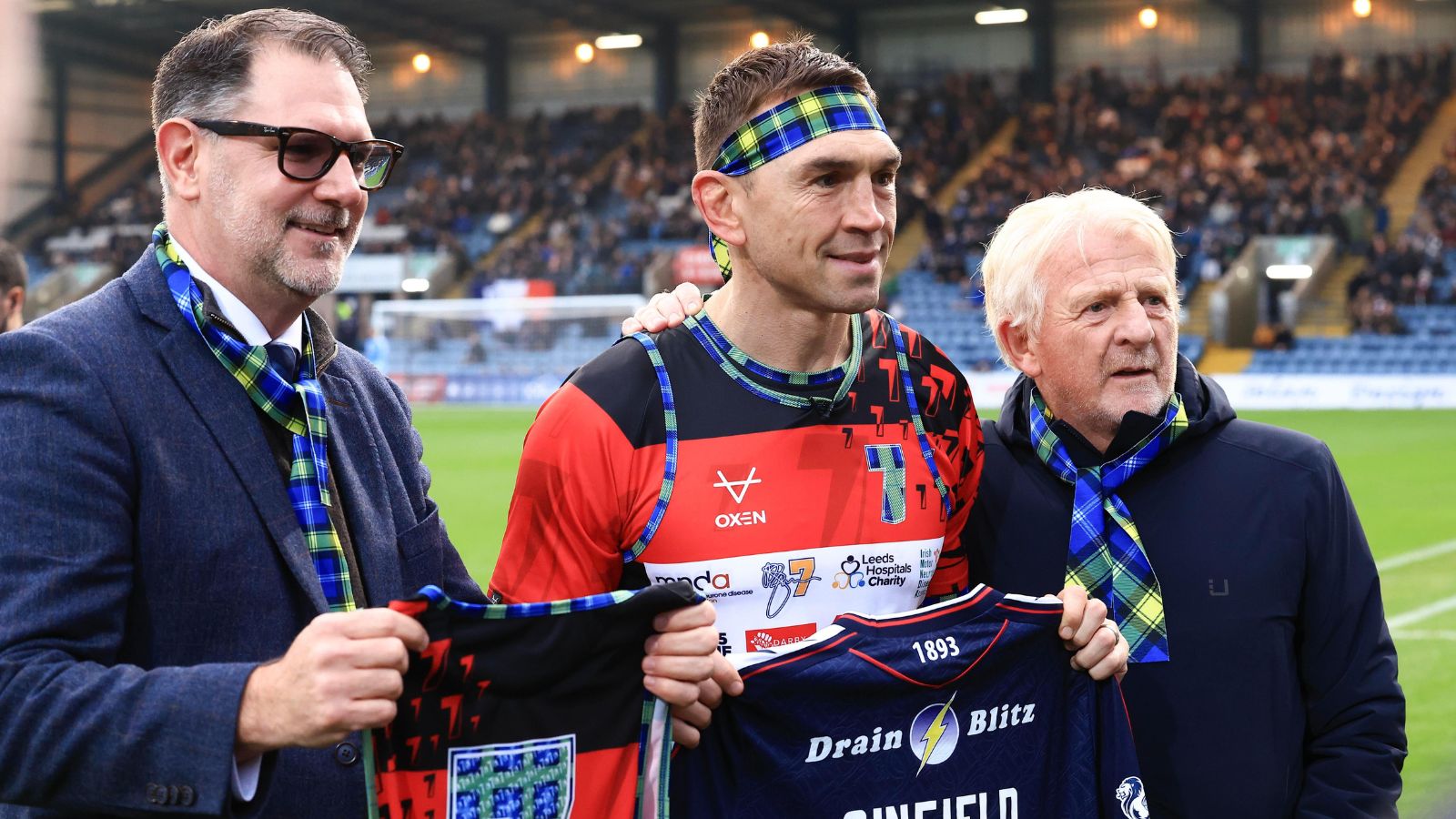 Kevin Sinfield is presented with a Dundee FC shirt by their managing director John Nelms and technical director Gordon Strachan pitchside at Dens Park after completing his sixth ultra-marathon during his '7 in 7: Together' challenge in 2025