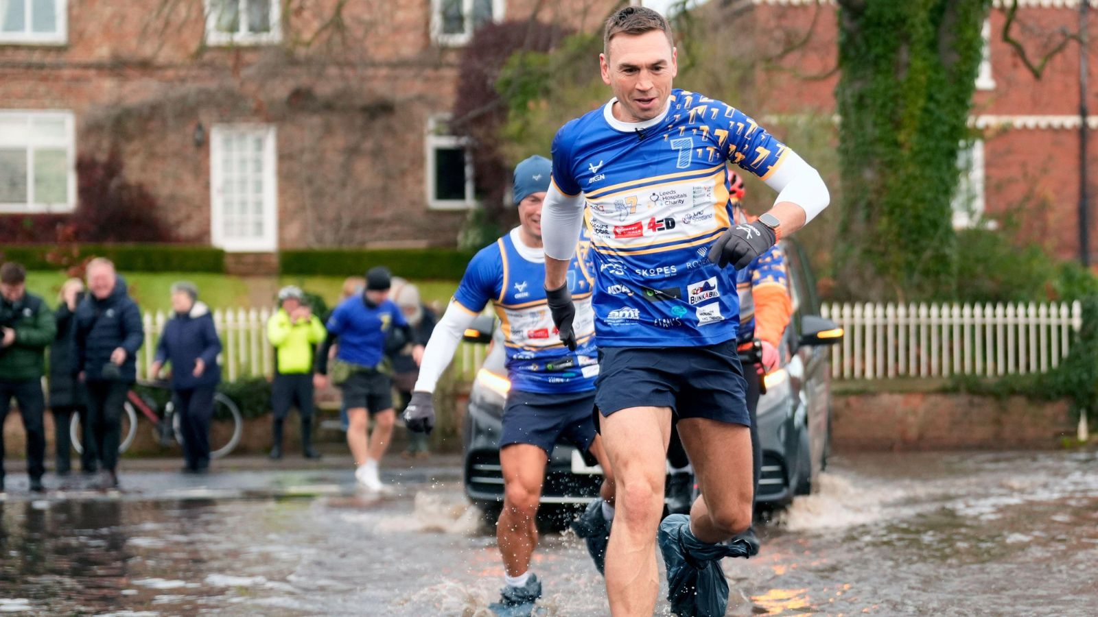 Kevin Sinfield sports bin bags over his trainers as he runs through flood water in Cattal during the final day of his '7 in 7: Together' challenge in 2025