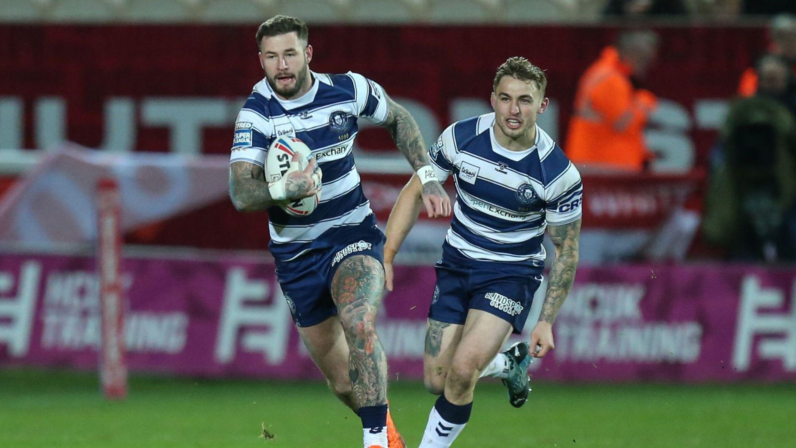 Zak Hardaker in action for Wigan Warriors away against Hull KR in Round 1 of the 2022 Super League season, carrying the ball with team-mate Sam Powell close behind supporting him