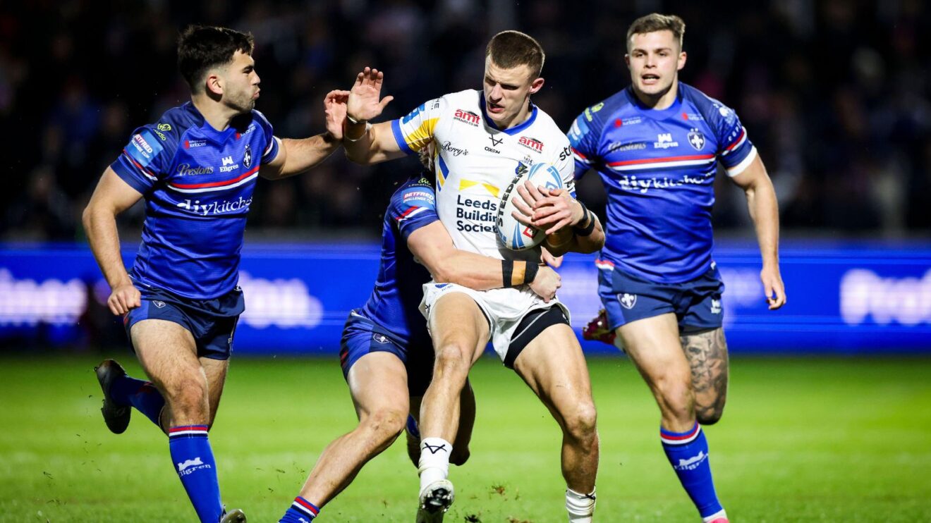 An action shot from the Challenge Cup Fourth Round tie between Wakefield and Leeds in 2026, with Rhinos captain Ash Hadley fending off three Trinity defenders